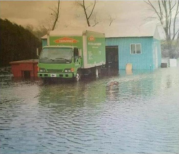 Green SERVPRO truck driving down flooded road.